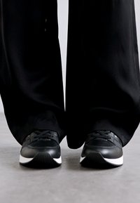 Sorte sneakers med en tekstureret overflade, der har en hvid sål og snørebånd. Kombineret med brede sorte bukser, der fremhæver et strømlinet og minimalistisk design.