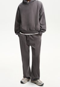 Grå sweatshirt med huva, avslappnad passform och ribbade ärmslut; matchande grå sweatpants med dragsko och sidostygn. Avslappnade skor.