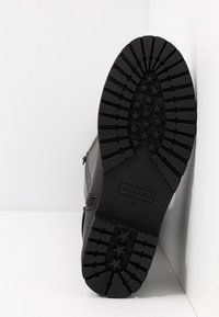 Sort støvlesål med stjerneformede slidbanemønstre og "Anna Field 37" prægede, fotograferet mod en hvid hjørnebaggrund.