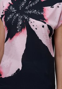 Kortärmad topp i lätt material, med en svart, rosa och vit blommönstring i metalliska accenter och en smidig yta.