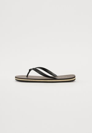 Fekete papucs, textúrált barna talpbetéttel, vékony fekete pántokkal és egy diszkrét fehér akcentussal a talp szélein.