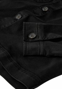 Close-up van zwarte stof met zichtbare knopen en gedetailleerde stiksel op een mouw en de voorkant van een shirt.