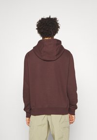 Burgundy huvtröja med mjuk textur, som har en känguruficka och ribbad nederkant, ihop med ljusgröna cargobyxor.