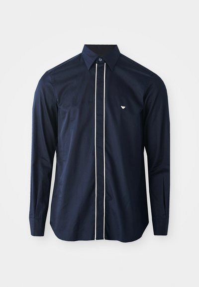 Camisa de manga larga navy de algodón con un cuello clásico, que presenta un ribete blanco en la parte delantera y un pequeño logo en el lado izquierdo del pecho.