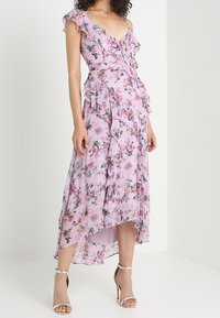 Blommig midiklänning i ljusrosa tyg med volangärmar, fallande volanger och skuren nederkant. Har en knappstängning fram och är knälång.