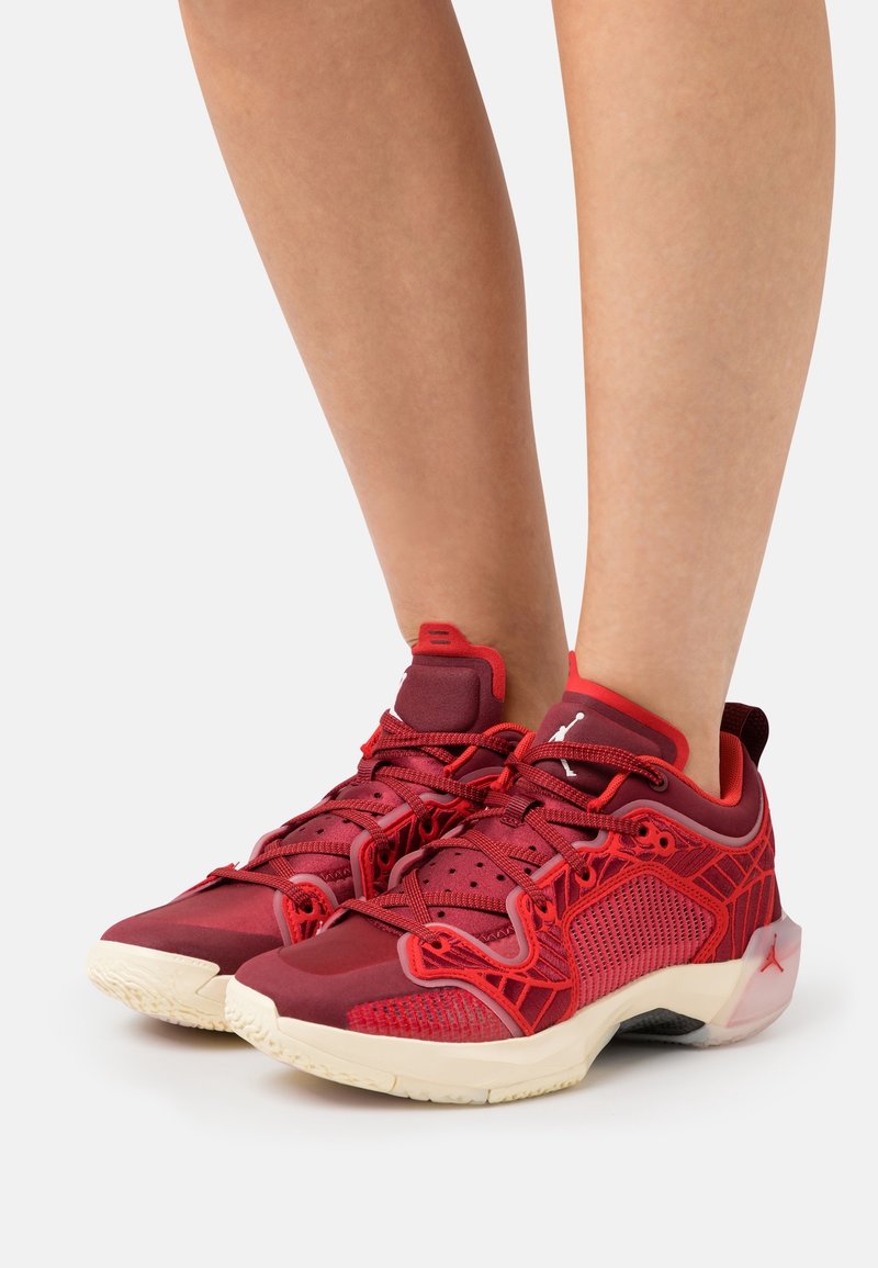 Paire de baskets de sport rouges avec des détails en mesh et texturés, portées pieds nus sur fond blanc.