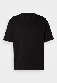 Black cotton t-shirt with short sleeves, featuring an embossed "Calvin Klein" logo on the front, round neckline, and a relaxed fit.