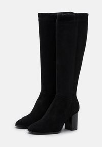 Un par de botas altas de ante negro con tacones cuadrados y puntas redondeadas sobre un fondo blanco.