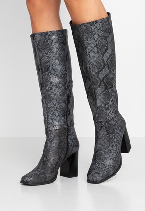 Knæhøje damesstøvler med gråt og sort slangeskindsmønster, spidse tæer, blokhæle og lynlåse på den indvendige side på en lys baggrund.