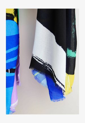 Stofstukken met abstracte ontwerpen in zwart, wit, blauw, geel, paars en groen, hangend tegen een effen lichte achtergrond.