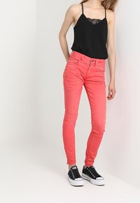 Rosa slim-fit jeans med fem fickor och bälteshällor, tillsammans med en svart linne med spetsdetaljer och svarta sneakers.