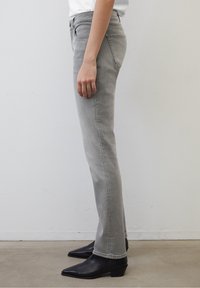 Jeans de mezclilla gris con corte recto y textura sutil, con una cintura de altura media y bolsillos laterales. Combinados con elegantes botines negros.