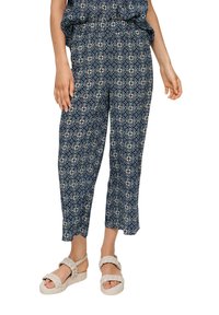 Marineblauwe broek met een geometrisch patroon, wijde pasvorm, cropped lengte en elastische tailleband, gecombineerd met lichtbeige plateausandalen.