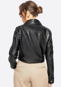 Giacca cropped in pelle nera con colletto classico e una leggera lucentezza. Presenta cuciture sartoriali e dettagli metallici sui polsini.