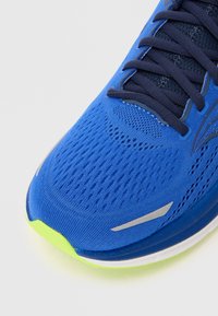 Scarpa sportiva blu con tomaia in mesh traspirante, dettagli a rilievo, accenti riflettenti e suola di un verde fluo.