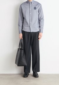 Grå knappad skjorta med broderad logotyp, svarta vida byxor och en svart tote-väska. Slät tyg med en strukturerad design.