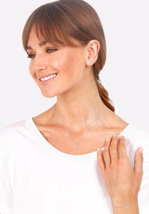 Ensemble de bijoux en argent comprenant des boucles d'oreilles en forme de cœur, un collier assorti et un bracelet. Le mannequin porte un top blanc et met en valeur des designs délicats.