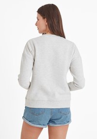 Light gray sweatshirt with a rounded neckline, soft texture, and long sleeves, paired with rolled denim shorts, viewed from the back.