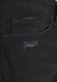 Černé džíny z denimu s texturovaným povrchem. Obsahují malou kapsu a ošuntělou část s třepenými okraji, které dodávají detail designu.