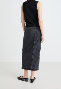 Svart ärmlös topp matchad med en lång, mörkgrå denimkjol med en slits bak och synliga söm detaljer, kompletterad med nitar på svarta skor.