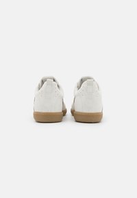 Weiße Wildleder-Sneaker mit einer strukturierten Oberseite, kontrastierenden Gummi-Laufsohlen in Kautschuk-Optik und Ziernähten. Zwei kleine Fersenschlaufen zum einfachen An- und Ausziehen.