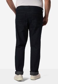 Pantalones de mezclilla oscura con un corte recto, que presentan dobladillos vueltos, dos bolsillos traseros y un acabado suave. Combinados con zapatillas claras.
