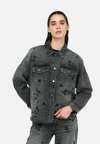 Graue Jeansjacke mit dekorativen schwarzen Perlenakzenten, zwei Brusttaschen, Druckknopfverschluss und lässiger Passform.