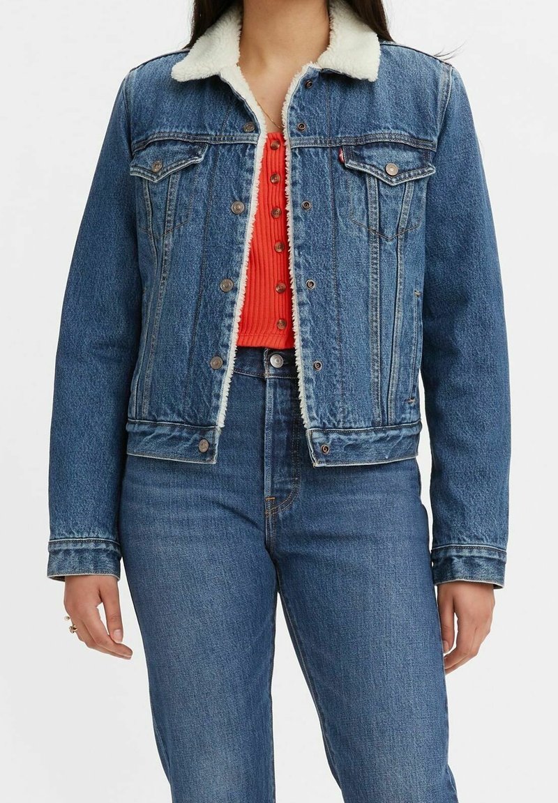 Chaqueta de mezclilla con un lavado azul claro, cuello de forro polar blanco, cierre de botones al frente, dos bolsillos en el pecho y un corte recto, combinada con una blusa roja.