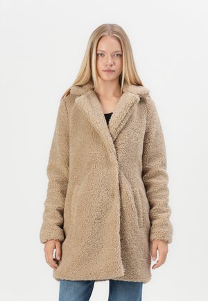 Manteau en fausse fourrure beige avec col à revers, manches longues et poches latérales, présentant une surface douce et texturée et un design mi-long.