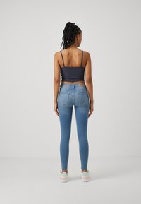 Vaqueros skinny azules de tiro alto, combinados con una camiseta de tirantes oscura ajustada. El material parece elástico. Los zapatos son blancos con acentos en pasteles.