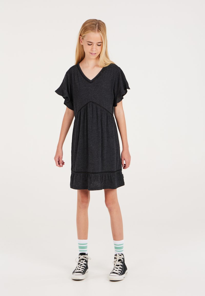 Dunkelgraues V-Ausschnittkleid mit kurzen Rüschensäumen, gerafftem Taillenbereich und abgestuftem Saum, getragen mit schwarzen High-Top-Schuhen und grün gestreiften Socken.