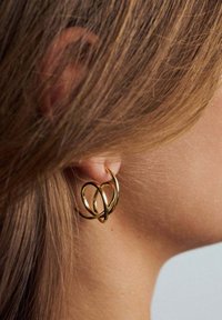 Gul hoopsörhängen med en vriden design, överlappande cirklar och en polerad finish. Bärs på örsnibben mot håret.