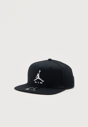 Casquette noire à visière plate avec logo Jumpman blanc et texte "AIR" brodé sur le devant, positionnée sur un fond clair uni.