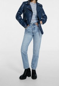 Veste de moto en cuir bleu marine sur un haut en dentelle bleu clair, assortie à un jean bleu clair taille haute et des bottines à plateforme noires.