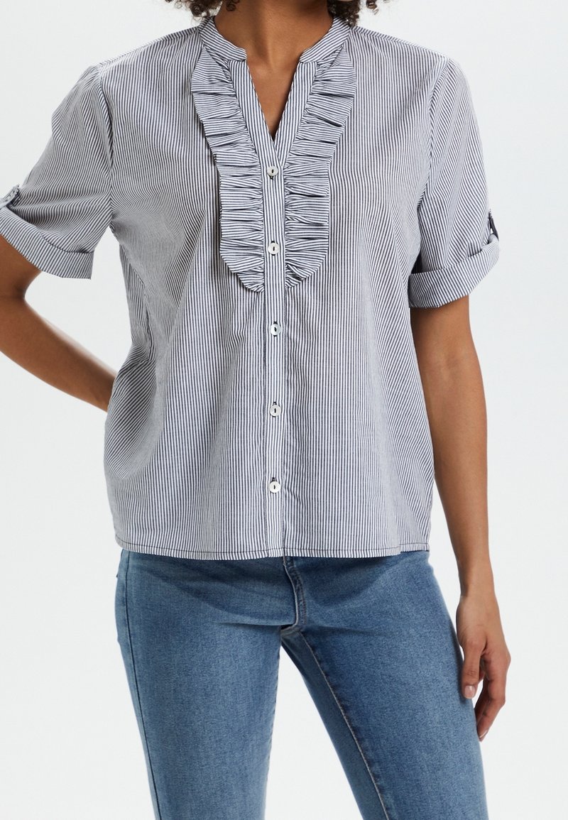 Blå och vit randig kortärmad skjorta med volangkant framtill och knäppning. Mjuk tygkvalitet, avspänt passform och uppvikta ärmar.