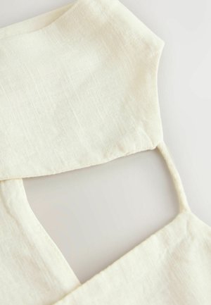 Close-up of cream-colored linen fabric with sleeveless garment straps and a square neckline on a light background.