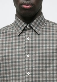 Camicia a quadri grigia e verde con colletto abbottonato, caratterizzata da bottoni bianchi e una texture morbida del tessuto.