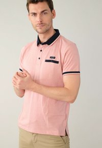Polo tričko s krátkym rukávom v svetloružovej farbe s námorníckym golierom a akcentmi na rukávoch. Obsahuje náprsné vrecko a trojrozpätkovú gombíkovú lištu. Materiál z bavlnenej zmesi.