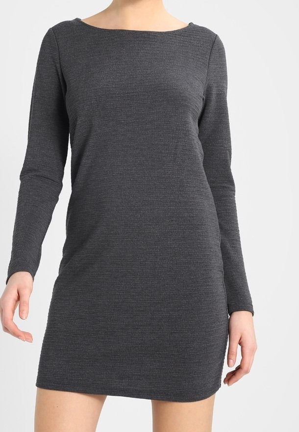Femme portant une robe en maille ajustée à manches longues, gris foncé, avec un col rond, debout devant un fond clair uni.