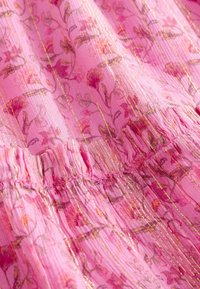 Roze stof met geplooide naad, bloemenpatroon en verticale gouden metalen strepen.