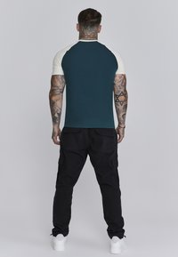 Heren T-shirt met een marineblauwe body en lichtcrème korte mouwen, gecombineerd met zwarte cargobroeken en witte sneakers, gezien vanaf de achterkant.