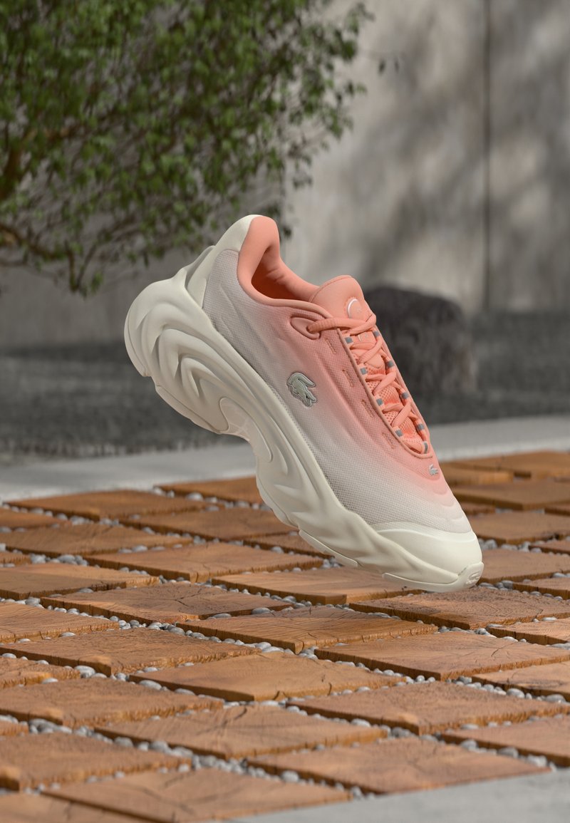 Baskets athlétiques rose clair et blanc avec une semelle épaisse flottant au-dessus d'un sol en bois et en carreaux de pierre à l'extérieur.