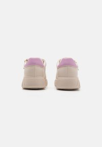 Sneakers bej cu o suprafață texturată și accente în violet la toc. Prezintă un guler căptușit și o talpă plată din cauciuc. Fără brand vizibil.