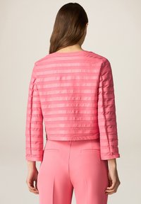 Giacca cropped rosa con un design a righe strutturato. Presenta maniche lunghe e un collo rotondo, abbinata a pantaloni rosa su misura.