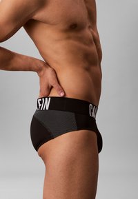 Boxer briefs neri con un frontale solido e un pannello in rete con un motivo a pois sul lato, contrassegnati da un elastico bianco con il marchio.