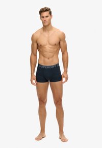 Boxers foncés en navy avec une ceinture grise "SUPERDRY", fabriqués dans un matériau doux, offrant une coupe ajustée et sans motifs visibles.