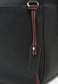 Mustasta teksturoidusta nahkabagista, jossa on hopeanvärinen vetoketju punaisella ja harmaalla raidallisella vetonauhallisella. Mukana on nahkaleima logotiedolla.