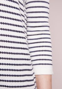 Witte gebreide top met marineblauwe horizontale strepen, een gestructureerd patroon en driekwart mouwen met een aangesloten boord.