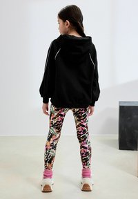 Svart huvtröja med vit kant, kombinerad med åtsittande leggings med ett flerfärgat kamouflage-mönster och rosa ankelstrumpor tillsammans med vita skor.