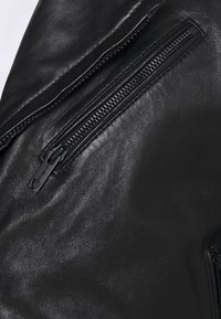 Zwarte leren jas met een close-up van een ritssluiting, met een gladde textuur en stevige zwarte ritssluitinghardware.